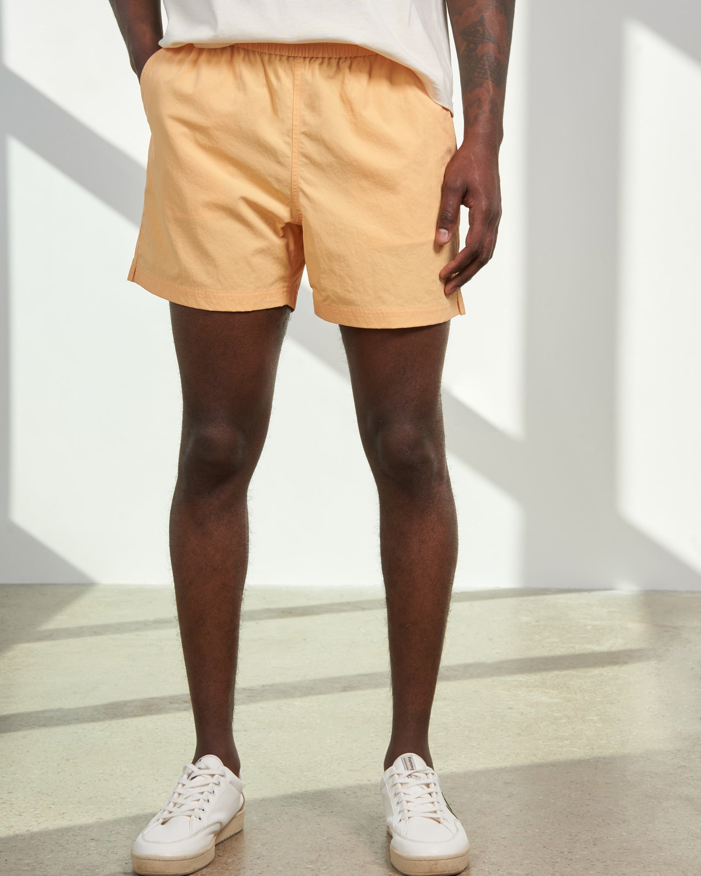 Buff Orange Recycled Sport Short (Front): Light orange elastic-waist shorts with side slits, worn with white sneakers