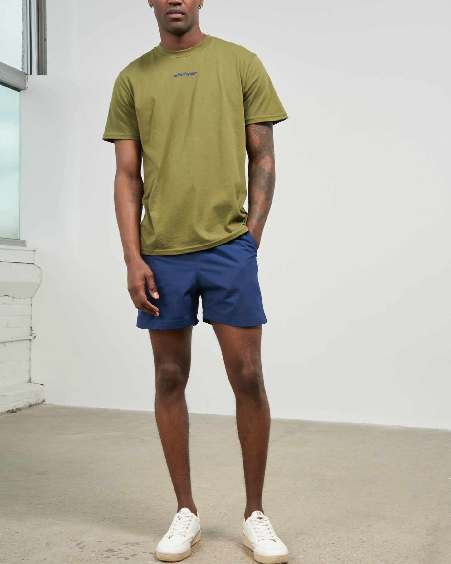 Estate Blue Recycled Sport Short (In-use): Man wearing navy blue shorts with olive green tee and white sneakers