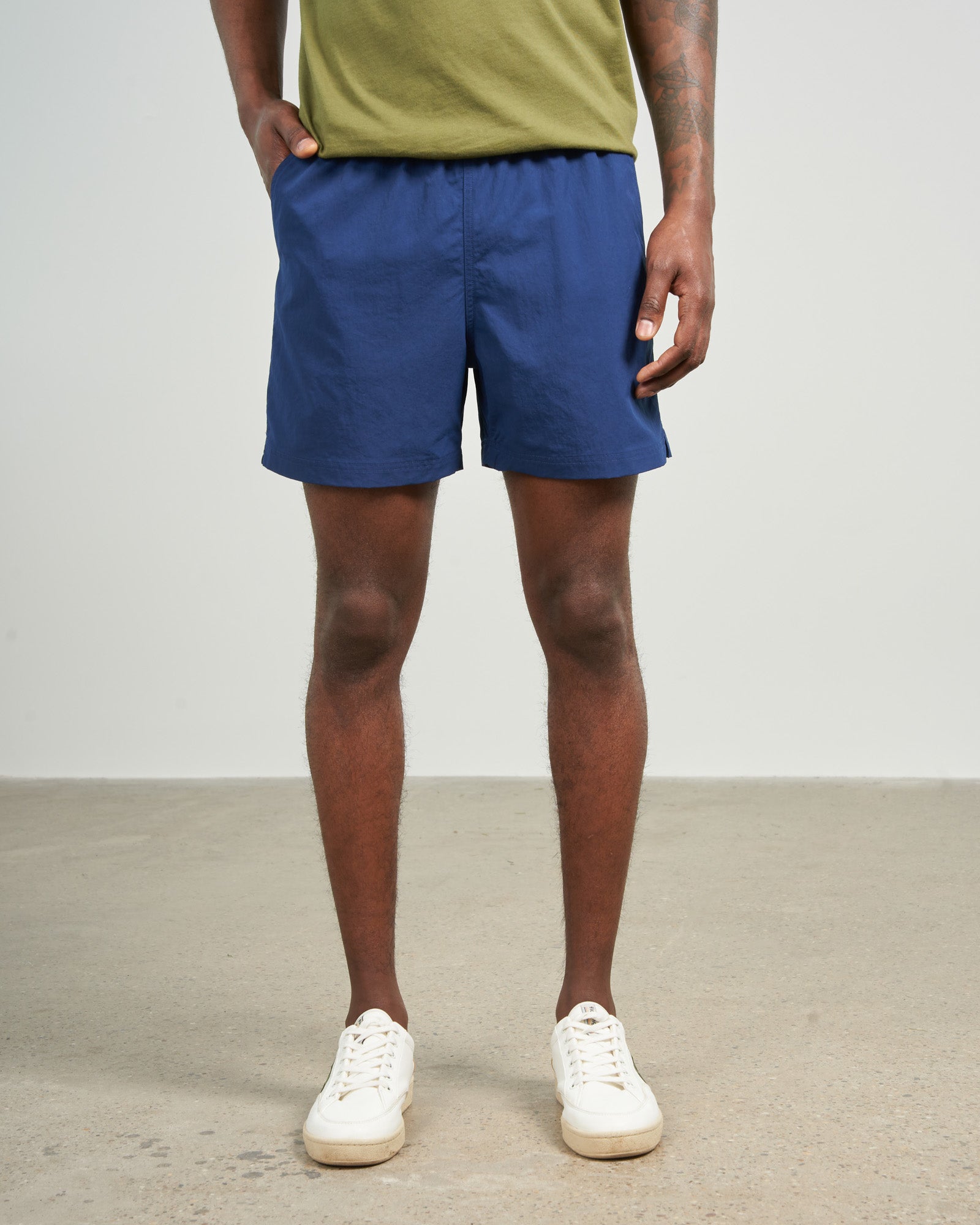 Estate Blue Recycled Sport Short (Front): Navy blue elastic-waist shorts with side pockets, worn with white sneakers