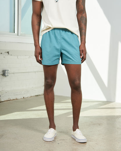 Teal Recycled Sport Short (In-use): Man wearing teal elastic-waist shorts with white sneakers outdoors