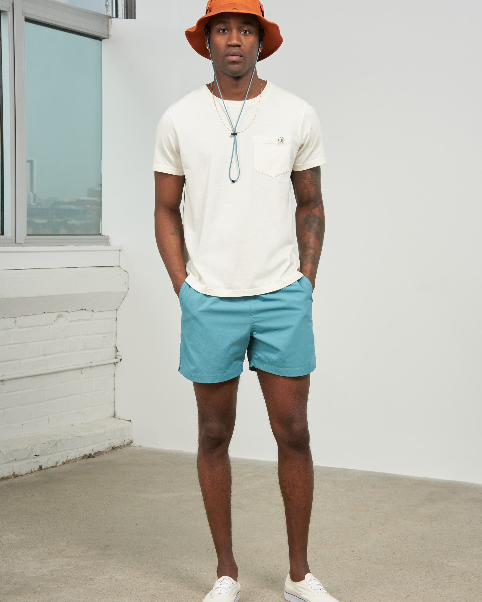 Teal Recycled Sport Short (In-use): Man wearing teal shorts with cream tee and orange bucket hat