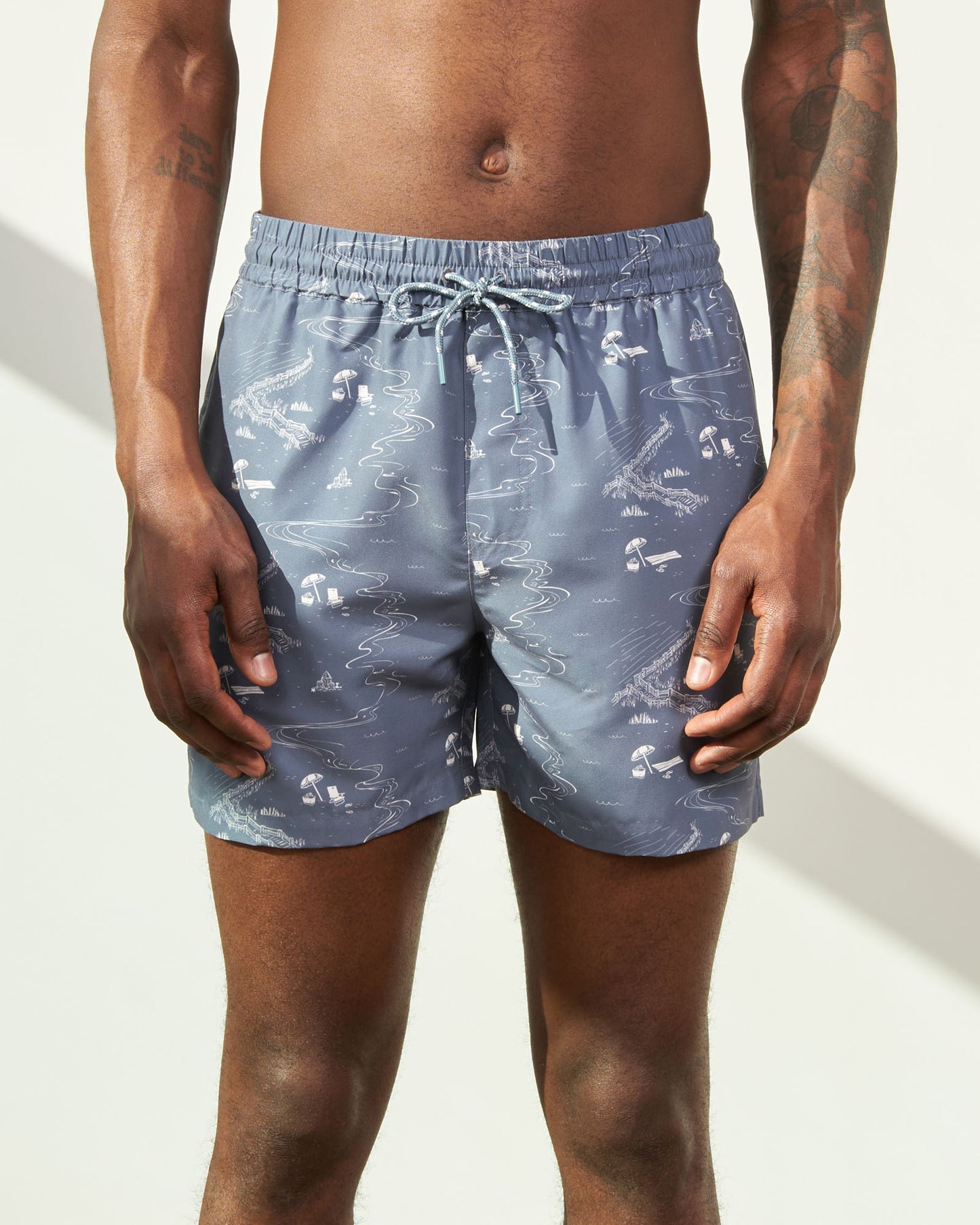 Stone Blue Recycled Swim Trunk - 5" (In-use): Blue-gray swim trunks with beach scene print and light blue drawstring