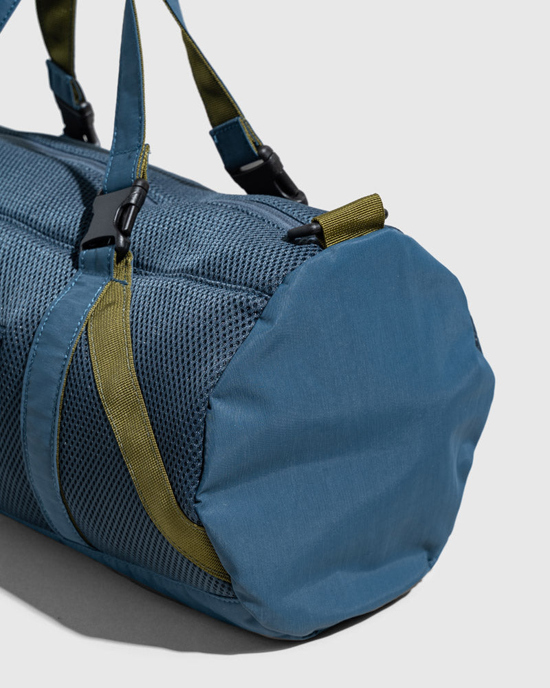 Blueberry (Re)active™ 16L Mini Duffle (Detail): Close-up of blue cylindrical duffle end panel with olive green straps and buckle