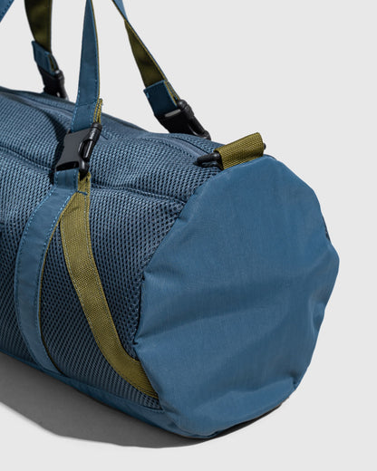 Blueberry (Re)active™ 16L Mini Duffle (Detail): Close-up of blue cylindrical duffle end panel with olive green straps and buckle