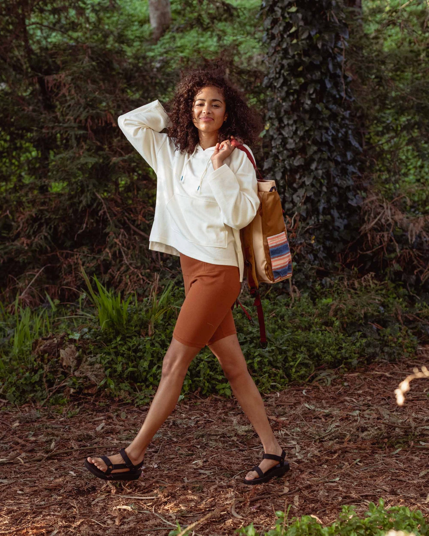 Cinnamon EcoKnit™ Ribbed Bike Short (In-use): Woman wearing rust-colored bike shorts with white hoodie in forest setting