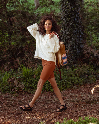 Cinnamon EcoKnit™ Ribbed Bike Short (In-use): Woman wearing rust-colored bike shorts with white hoodie in forest setting