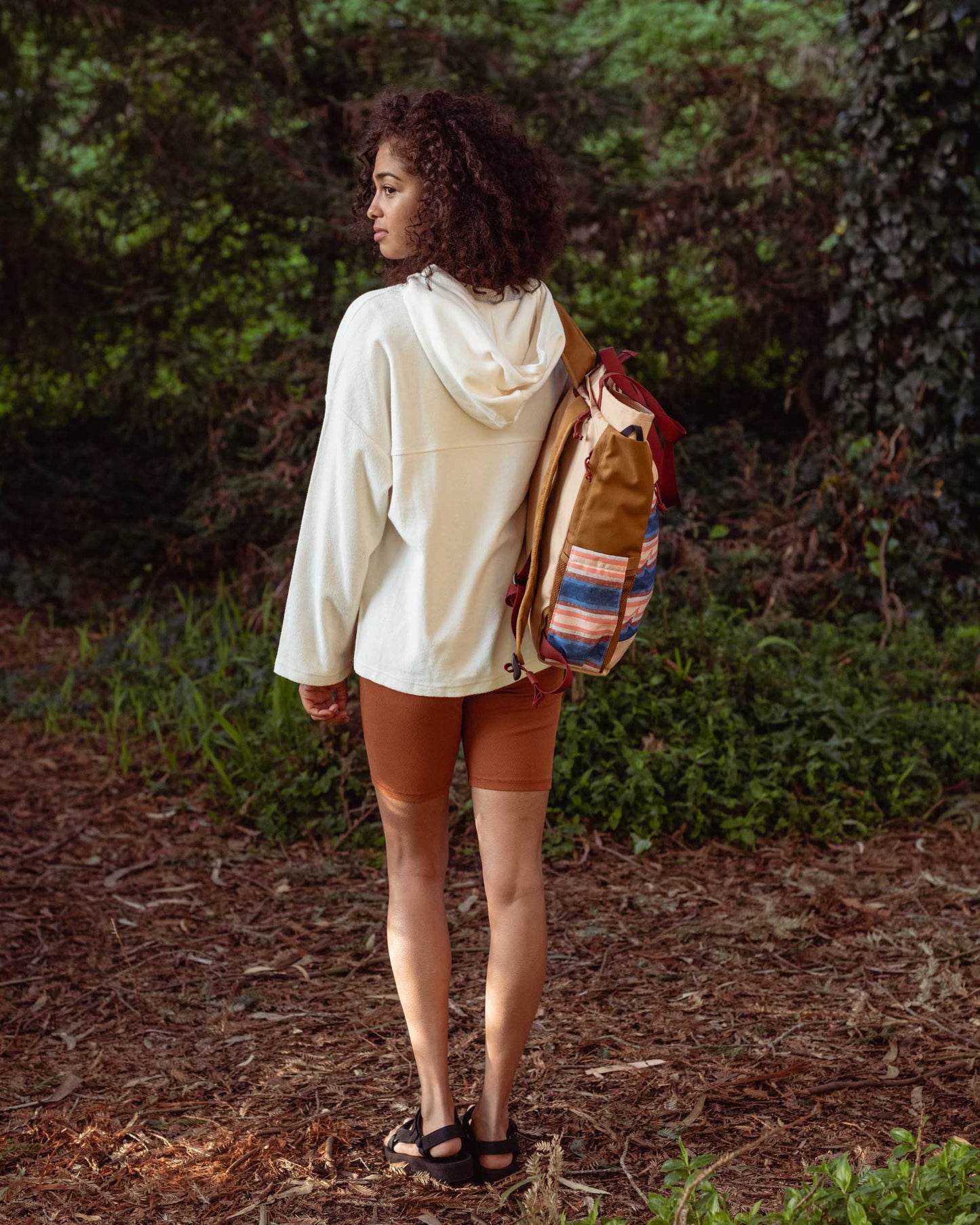 Cinnamon EcoKnit™ Ribbed Bike Short (In-use): Woman in forest wearing rust-colored bike shorts with white hoodie and backpack