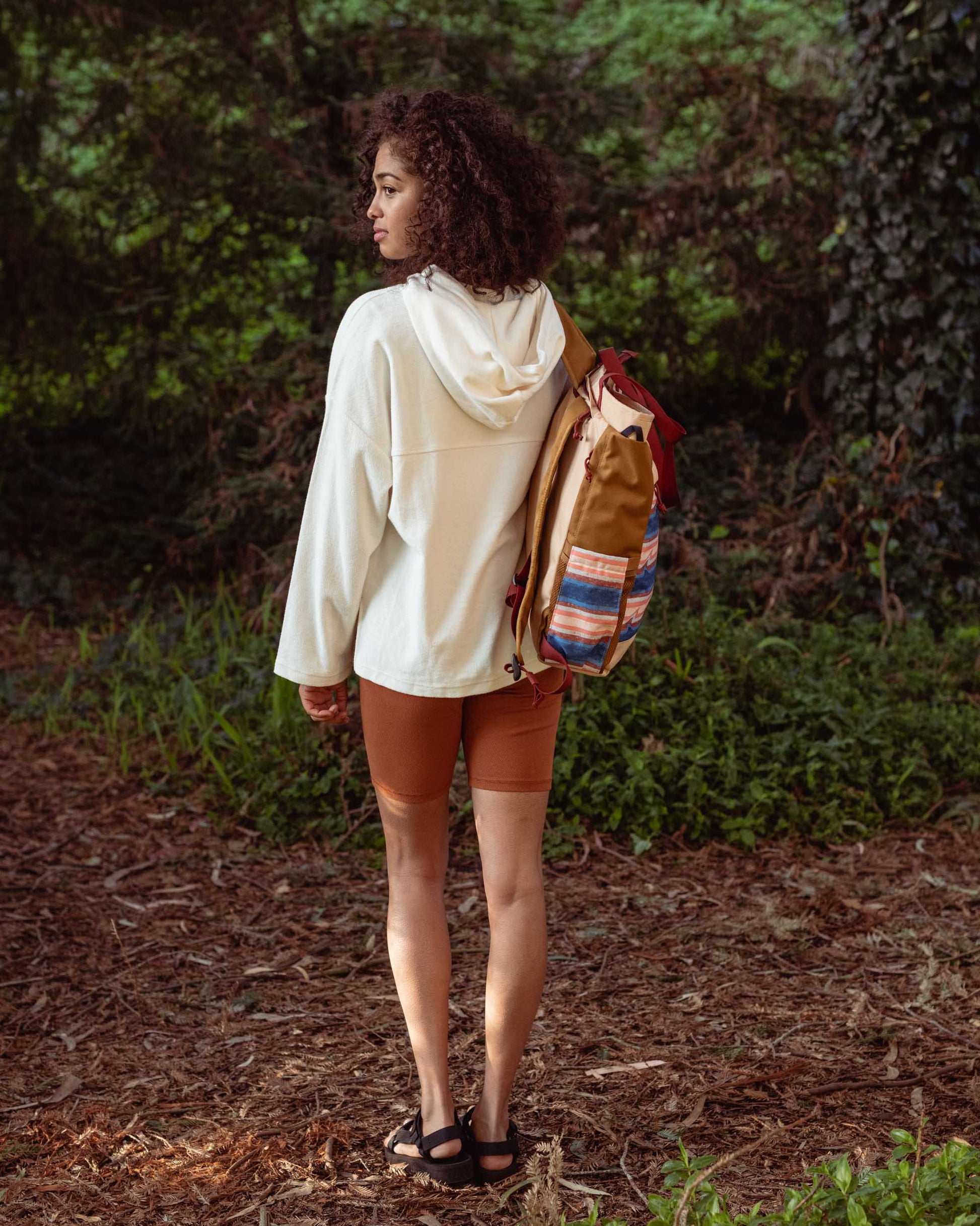 Cinnamon EcoKnit™ Ribbed Bike Short (In-use): Woman in forest wearing rust-colored bike shorts with white hoodie and backpack