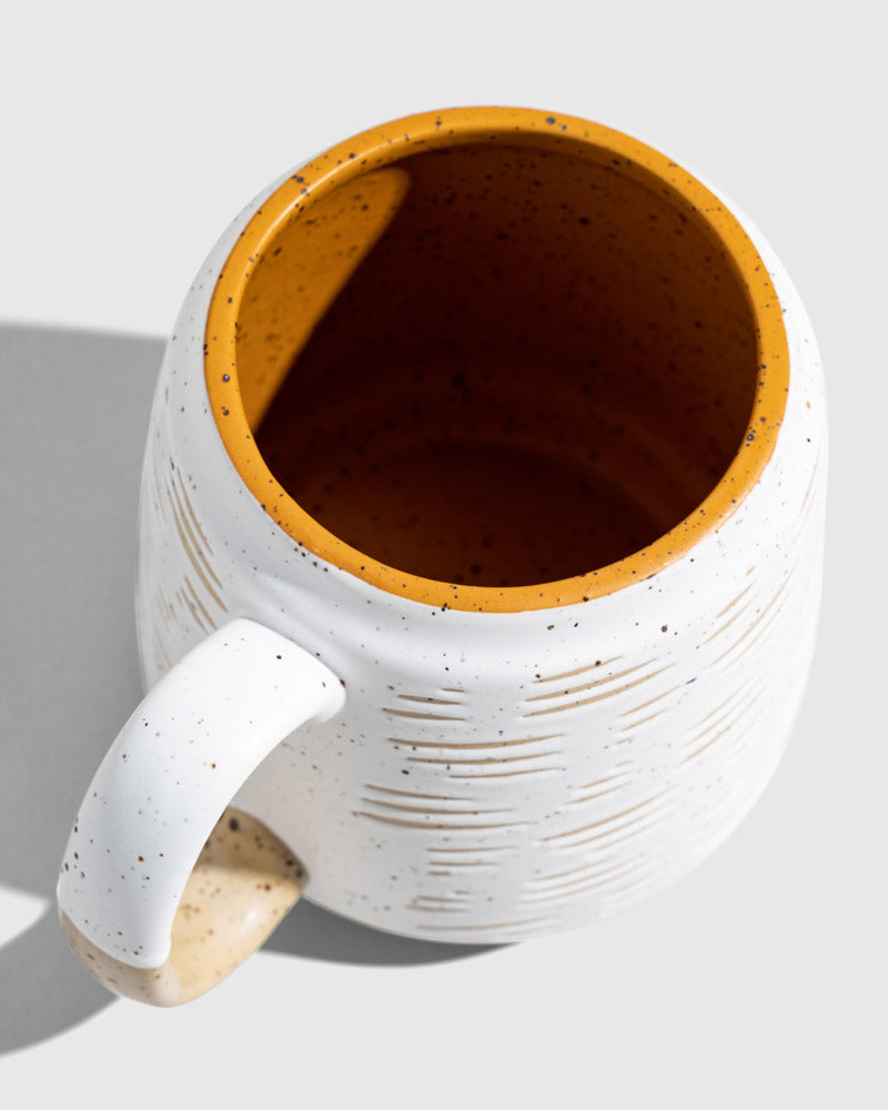 Eggshell 16 oz. Stoneware Mug (Detail): Top-down view showing yellow interior rim and speckled white exterior with texture lines