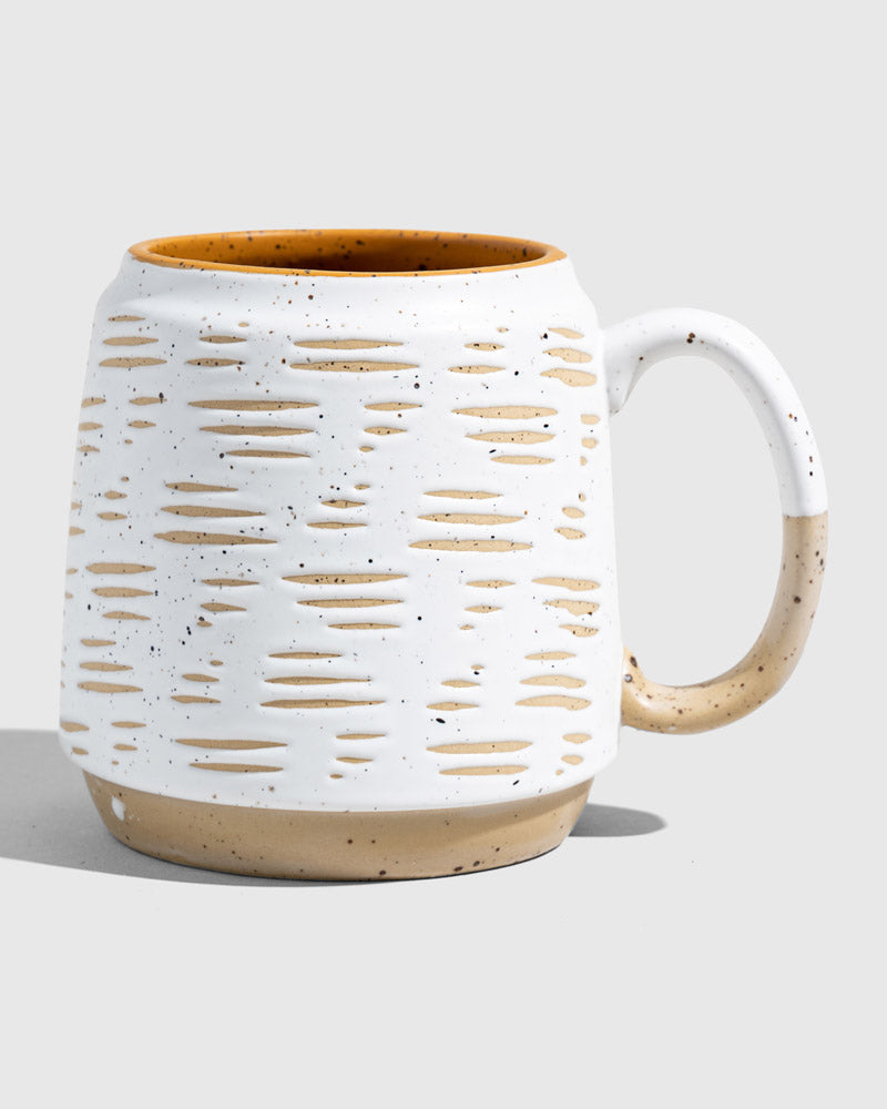 Eggshell 16 oz. Stoneware Mug (Angle): White speckled mug with oval cutout pattern, tan base, mustard interior