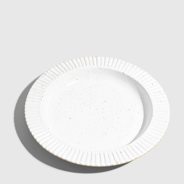 Eggshell Stoneware Stackable Plate (Angle): Round white speckled plate with ribbed fluted rim, unglazed edge visible
