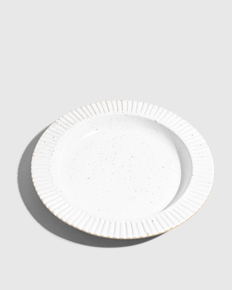 Eggshell Stoneware Stackable Plate (Angle): Round white speckled plate with ribbed fluted rim, unglazed edge visible