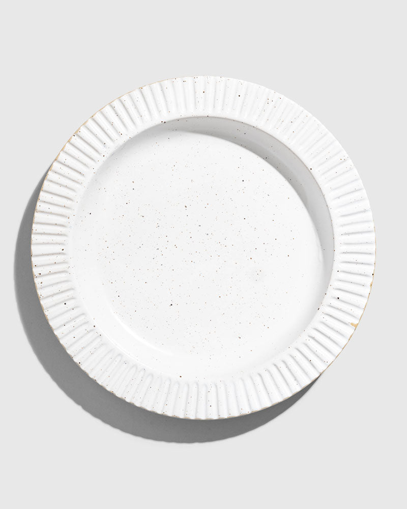 Eggshell Stoneware Stackable Plate (Flat-lay): Round white speckled plate with ribbed fluted rim and subtle gold edges