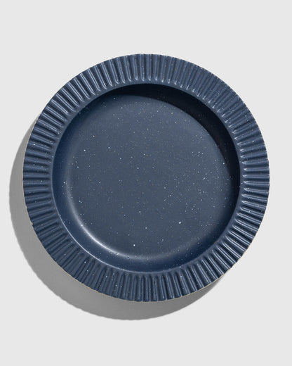 Slate Stoneware Stackable Plate (Flat-lay): Round dark blue speckled plate with ribbed fluted rim, overhead view
