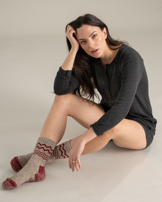 Red The Ultimate Bison Wool Sock (In-use): Woman seated on floor wearing tan and red zigzag wool crew socks