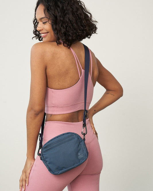 Deep Sea (Re)active™ 2L Convertible Crossbody (In-use): Woman in pink athletic wear carries small navy blue crossbody bag