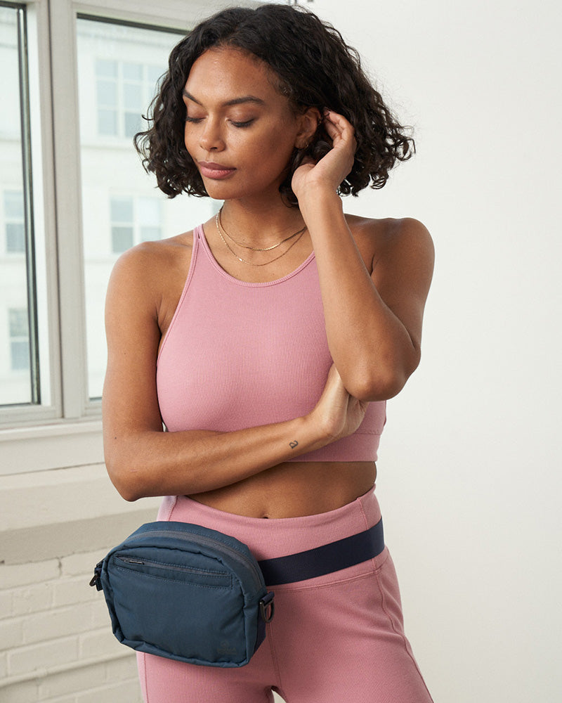 Deep Sea (Re)active™ 2L Convertible Crossbody (In-use): Woman wearing navy belt bag around waist in bright studio setting