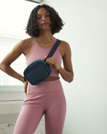 Deep Sea (Re)active™ 2L Convertible Crossbody (In-use): Woman in pink athleisure wearing navy crossbody bag with wide strap